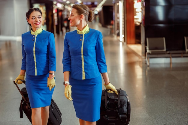 Agents de bord souriants transportant des sacs de voyage à l'aéroport