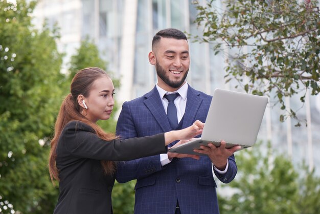 Des agents immobiliers d'hommes d'affaires et de femmes d'affaires avec un ordinateur portable à l'extérieur, des entrepreneurs kazakhs asiatiques discutent d'un projet