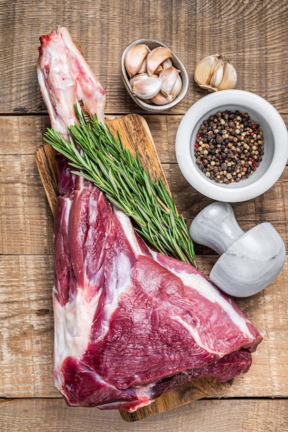 Agneau cru frais ou jambe de chèvre au romarin et au poivre sur une planche à découper. fond en bois. Vue de dessus.