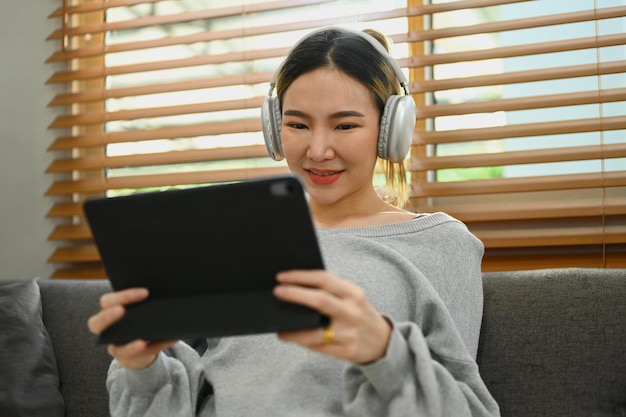 Agréable jeune femme portant un casque en regardant une vidéo en naviguant sur Internet ou en faisant des achats en ligne via une tablette numérique