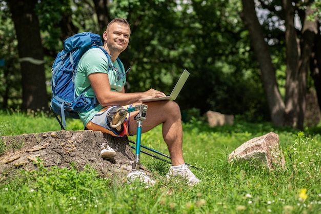 Agréable jeune homme souriant profitant de ses journées touristiques tout en utilisant son ordinateur portable