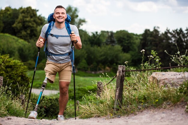 Agréable touriste masculin tenant des bâtons de marche nordique tout en se sentant enthousiaste malgré des problèmes de santé