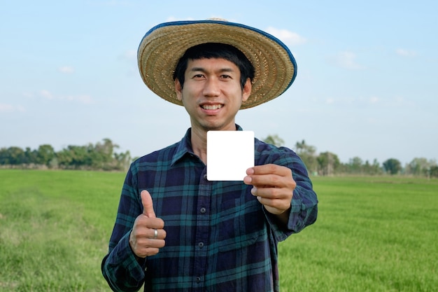 Agriculteur asiatique tenant une carte en papier blanc et souriant pouce vers le haut à la ferme de riz