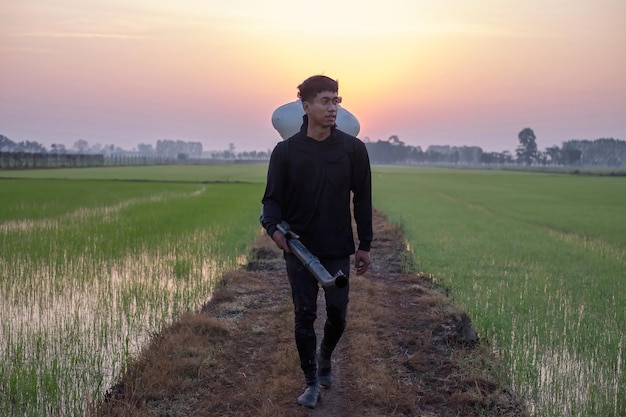 Un agriculteur asiatique utilise un Knapsack Mist Duster pour planter des engrais chimiques sur sa ferme de riz vert