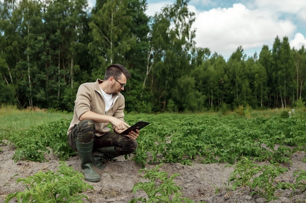 Un agriculteur assis dans le champ et en utilisant une tablette. Application moderne des technologies dans les activités agricoles.