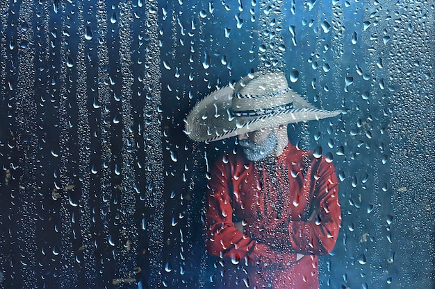 agriculteur dans un chapeau de paille derrière des gouttes de pluie en verre, météo saisonnière de l'ouest sauvage de l'amérique