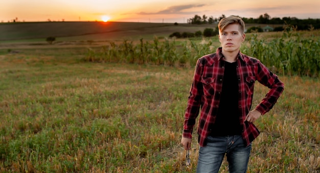 Un agriculteur dans une chemise se dresse dans un champ au coucher du soleil