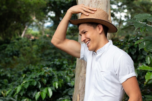 Agriculteur dans une plantation de café avec un chapeau souriant. Propriétaire de ferme observant ses récoltes de café