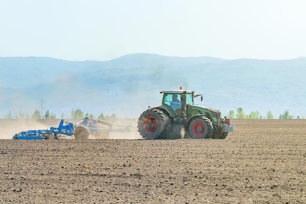 Agriculteur dans le tracteur préparant le cultivateur de lit de semence de terre. Paysage de tracteur agricole.