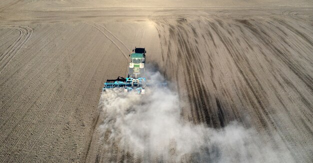 Un agriculteur dans un tracteur prépare la terre avec un cultivateur de semis dans le cadre des travaux de pré-semis au début de la saison agricole de printemps sur les terres agricoles.