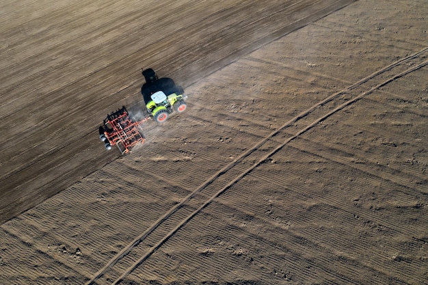 Un agriculteur dans un tracteur prépare la terre avec un cultivateur de semis dans le cadre des travaux de pré-semis au début de la saison agricole de printemps sur les terres agricoles.