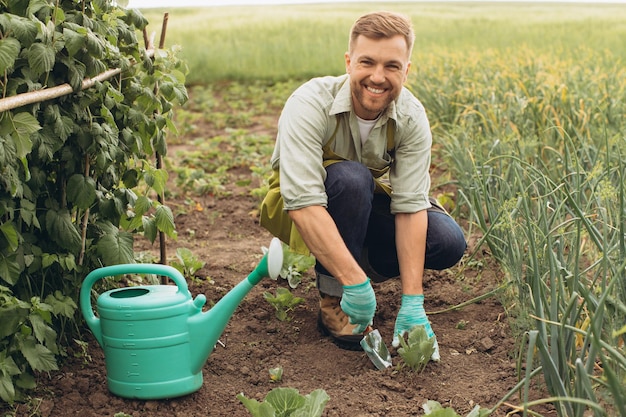 Un agriculteur heureux arrose les lits et travaille dans le jardin