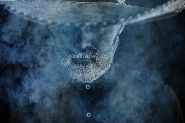 Agriculteur hipster dans un chapeau de paille avec bord en fumée fumer du tabac style rétro sambrero sauvage de l'ouest