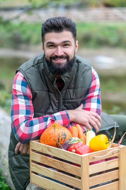 Agriculteur. Un homme aux cheveux noirs en chemise à carreaux avec une boîte de légumes