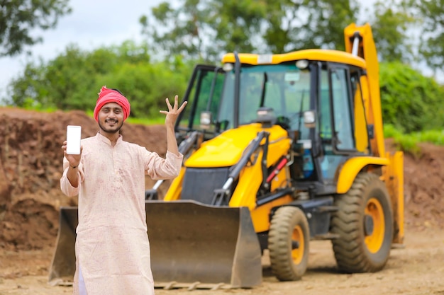 Agriculteur indien montrant un smartphone avec son nouvel équipement de machine de terrassement