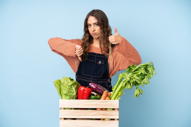 Agriculteur avec des légumes fraîchement cueillis dans une boîte faisant bon-mauvais signe. Indécis entre oui ou non
