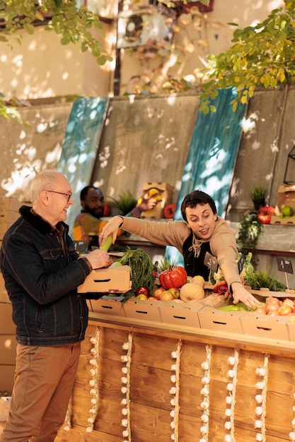 Agriculteur local souriant vendant des produits bio naturels frais, donnant des fruits et légumes du marché alimentaire à un ancien client. Vendeuse parlant à un homme âgé de divers produits sains de saison.