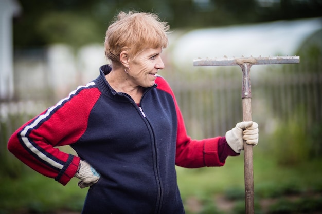 L'agriculteur se tient avec un râteau dans le jardin Préparation du sol pour la plantation de légumes Concept de jardinage Travail agricole sur la plantation