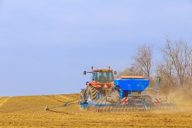 Un agriculteur avec un semoir sur un tracteur - semant du grain dans un domaine agricole. Cultiver du blé.