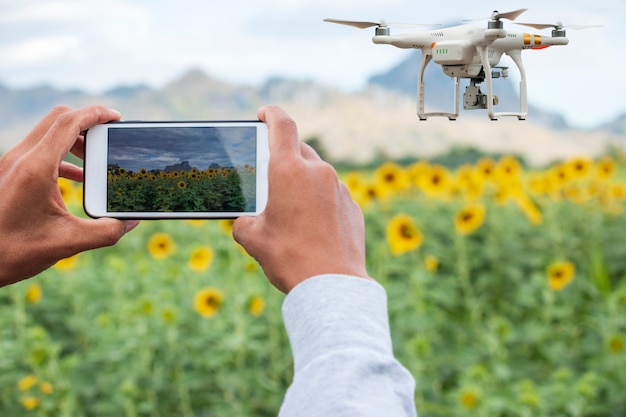 Agriculteur avec téléphone intelligent sur le terrain avec drone volant au-dessus des terres agricoles