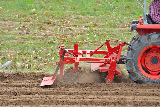 Agriculteur en tracteur labourant la terre avec un tracteur rouge pour l'agriculture