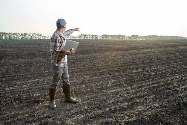 Agriculteur travaillant sur son ordinateur portable dans le domaine de la planification de l'agriculture Innovations agroalimentaires