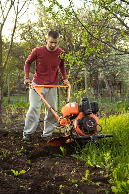 Un agriculteur travaille dans le champ labourant la terre avec une charrue à la ferme Un laboureur en promenade derrière un motoculteur Saison de travail du sol Culture biologique de produits naturels Agriculture