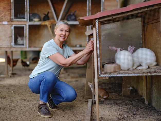 Une agricultrice adulte avec des lapins blancs dans sa ferme. L'agriculteur s'occupe des animaux.