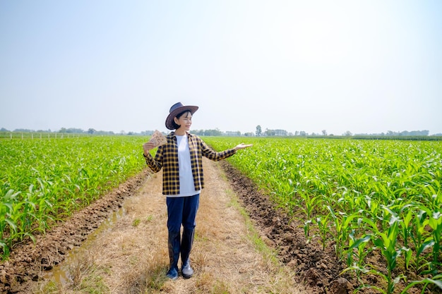 Une agricultrice asiatique dans une chemise rayée portant un chapeau posant debout avec des factures de revenu de maïs