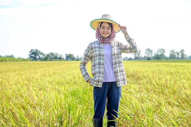 Agricultrice asiatique portant une chemise rayée portant un chapeau debout et posant avec un visage souriant à la rizière