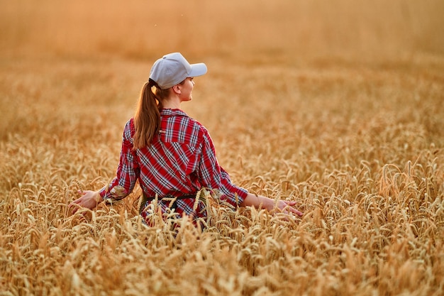 Agricultrice debout dans un champ de blé sec jaune doré et regardant au loin