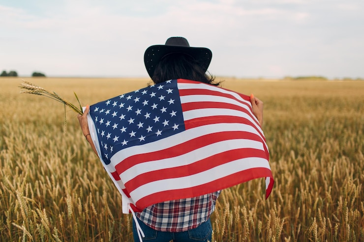 Photo agricultrice portant chapeau de cow-boy chemise à carreaux et jeans avec drapeau américain au champ de blé