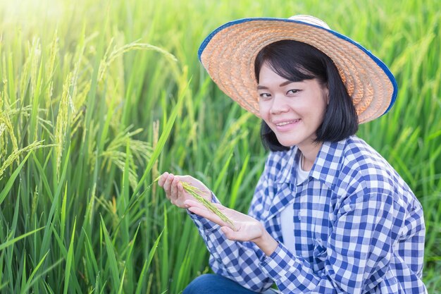 Une agricultrice portant une chemise rayée est assise avec du riz paddy dans une belle rizière verte.