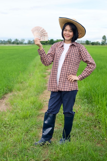 Une agricultrice porte un chapeau posant avec des billets souriant dans une rizière