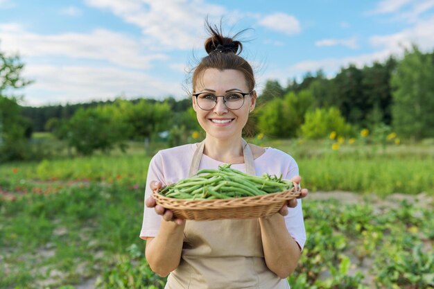 Agricultrice souriante avec récolte de haricots verts frais dans un panier Potager d'été fond de ciel bleu de plus en plus d'aliments sains biologiques naturels