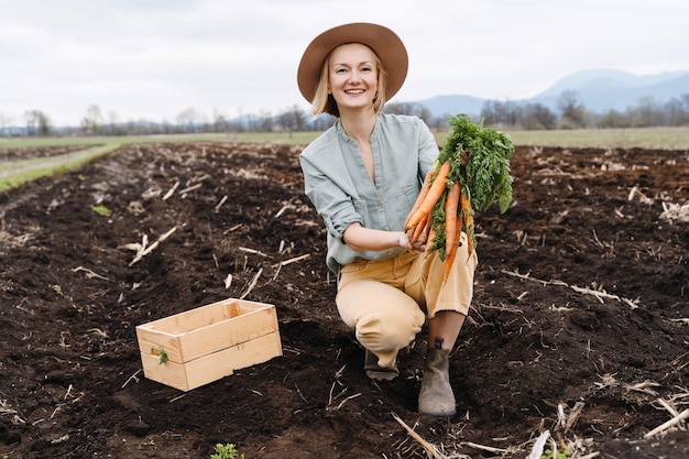 Agricultrice tenant une boîte en bois remplie de légumes crus frais dans un champ agricole