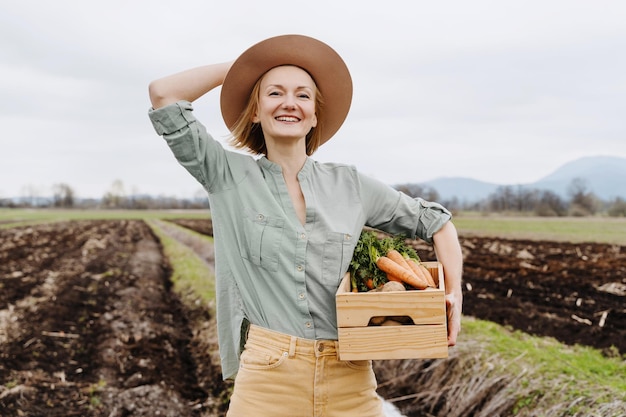 Agricultrice tenant une boîte en bois remplie de légumes crus frais dans un champ agricole