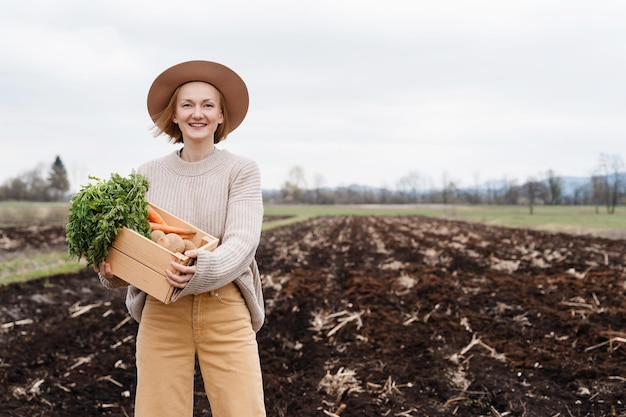 Agricultrice tenant une boîte en bois remplie de légumes crus frais dans un champ agricole