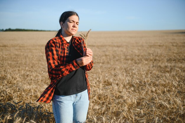 Une agricultrice travaillant dans un champ de blé au coucher du soleil Une femme d'affaires agronome se penche sur une tablette dans un champ de blé