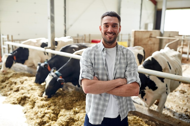 agriculture, industrie, agriculture, personnes et élevage - concept de jeune homme ou d'agriculteur heureux et souriant avec un troupeau de vaches dans un étable d'élevage laitier