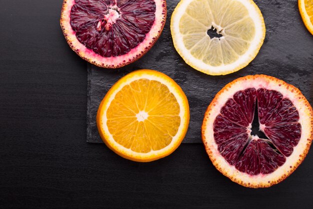 Agrumes frais et mûrs. Citrons, oranges rouges et oranges sur table en pierre sombre. Espace copie