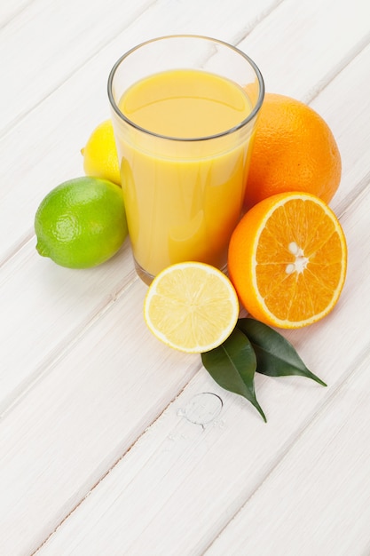 Agrumes et verre de jus. Oranges, limes et citrons. Sur fond de table en bois blanc