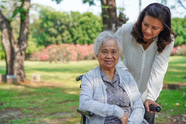 L'aidant aide et soutient une vieille dame asiatique âgée ou âgée patiente en fauteuil roulant dans le parc sain concept médical fort