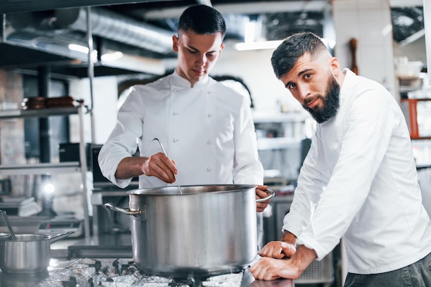 Avec l'aide d'un autre employé Chef en uniforme blanc cuisinant des aliments à la cuisine Journée bien remplie au travail