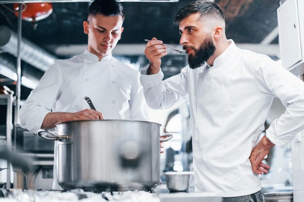 Avec l'aide d'un autre employé Chef en uniforme blanc cuisinant des aliments à la cuisine Journée bien remplie au travail