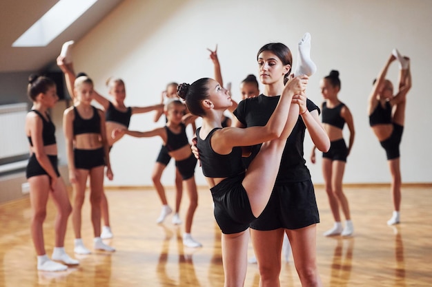 Avec l'aide d'un entraîneur Groupe d'enfants féminins pratiquant des exercices sportifs ensemble à l'intérieur