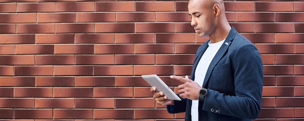 Photo À l'aide d'un gadget jeune homme debout sur le mur naviguant sur internet sur une tablette numérique vue latérale concentrée