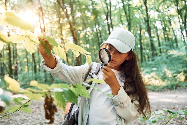 À l'aide d'une loupe, la fille est dans la forêt pendant la journée d'été à la découverte de nouveaux endroits