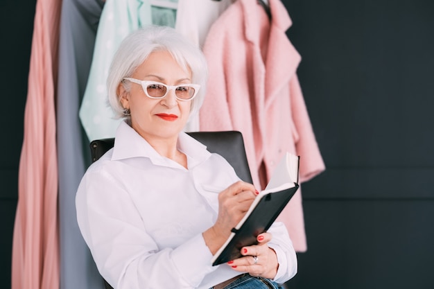 Aide à la mode. Mode de vie des seniors. Femme âgée confiante regardant la caméra tout en prenant des notes dans l'agenda.