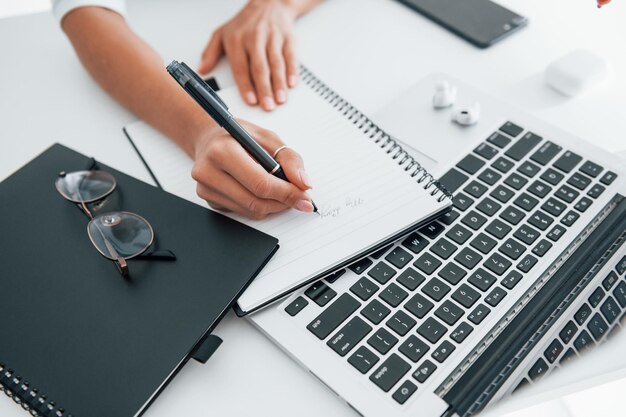 À l'aide d'un ordinateur portable et d'un bloc-notes Jeune femme indépendante travaillant à l'intérieur au bureau pendant la journée